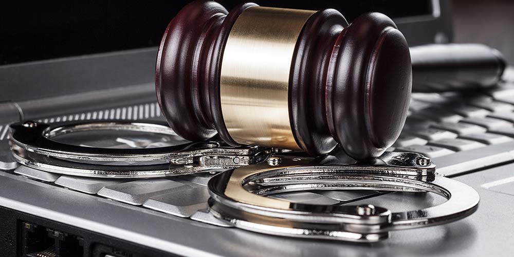 A gavel and handcuffs rest on a laptop keyboard, illustrating the concept of remote criminal proceedings during COVID-19 related social distancing