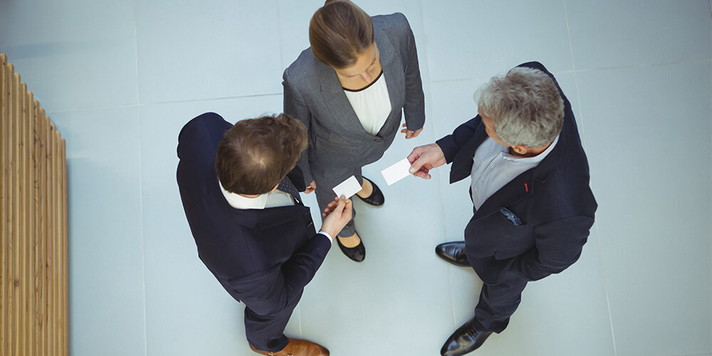 A trio of attorneys exchange business cards, which is a component of strong personal branding.