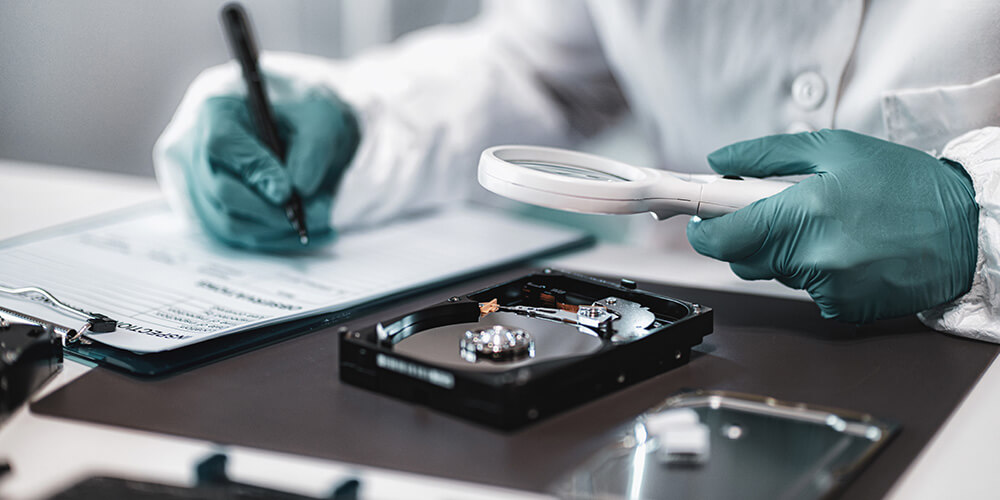 Photo of a forensic examiner inspecting a hard-drive and preparing a privileged forensic report.
