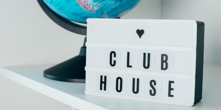 Concept photo of a lightbox sign in front of a globe with the word Clubhouse written on it.